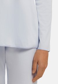 Ljusblå långärmad topp med en slät, mjuk textur och rundad nederkant, som matchas med ljusblå byxor.