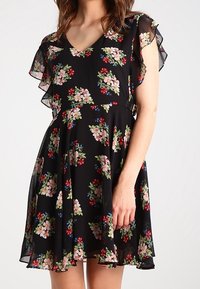 Robe noire à motifs floraux avec des manches courtes et volantées ; présente un décolleté en V et des motifs de fleurs colorées en rose, rouge et bleu sur un tissu fluide.