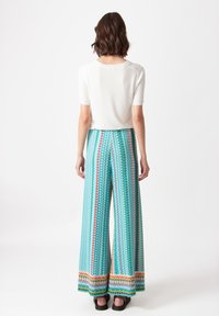 Witte top met korte mouwen gecombineerd met wijde, gestreepte broeken met turkooise, rode en gele accenten en een luchtige, lichte stof.