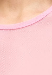 Κοντινό πλάνο στο άνω μέρος του στήθους και του λαιμού ενός ατόμου που φοράει ροζ τοπ από δίχτυ με στρογγυλή λαιμόκοψη.