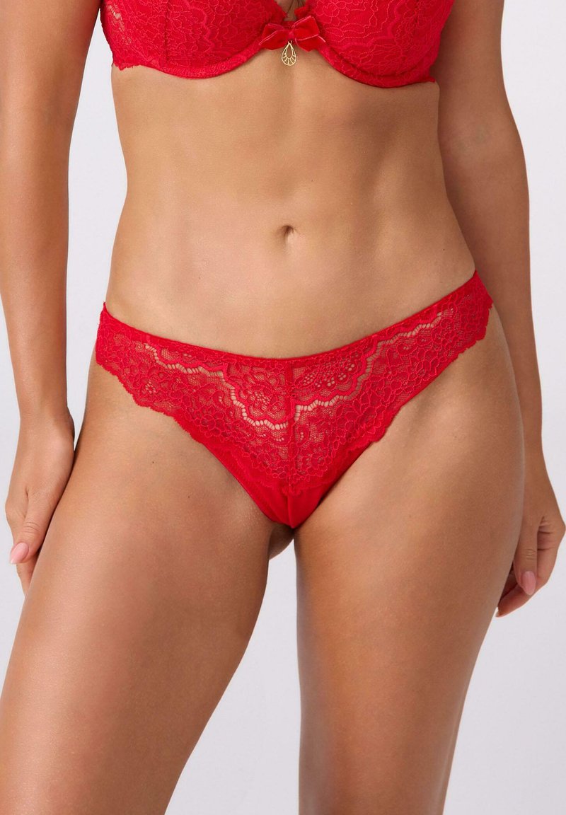 Czerwone koronkowe stringi z kwiatowym wzorem, z gładkim tyłem i kontrastującym pasem w talii. Ozdobione małym złotym detalem.