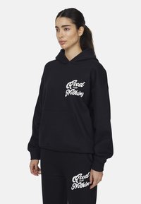 Felpa nera con tasca frontale, con testo bianco che recita "Good for Nothing." Il tessuto appare morbido con una vestibilità standard e cappuccio con stringhe.