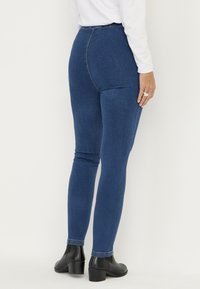 Blå denim skinny jeans med hög midja, slät textur och minimala sömnadsdetaljer, i kombination med svarta ankboots.