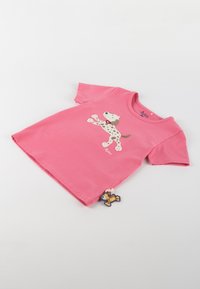 Pink cotton T-shirt with short sleeves featuring a cartoon dog print and a tag with a small lion character at the bottom corner.
