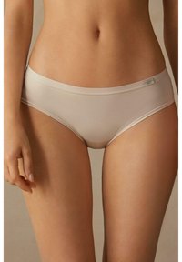 Slip hipster in cotone beige con elastiche morbide in vita, texture liscia, design senza cuciture e discreto logo laterale.