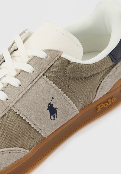 Αθλητικό παπούτσι casual με πάνελ από μπεζ σουέντ και καμβά, λευκά κορδόνια, σόλα gum με ανάγλυφο το λογότυπο "Polo" και λογότυπο παίκτη πόλο σε ναυτικό μπλε στο πλάι.