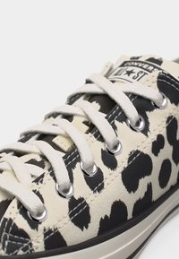 Αθλητικό παπούτσι Converse Chuck Taylor All Star με καμβά σε μαύρο και κρεμ με ζωοειδές σχέδιο και λευκά κορδόνια περασμένα από μεταλλικές τρύπες.