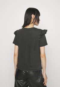 Camiseta negra con detalles de volantes en los hombros, mangas cortas y un corte relajado, hecha de un material de algodón suave. Diseño limpio en la parte posterior.
