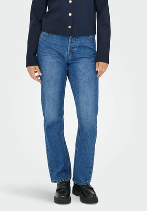 Jean en denim bleu avec une coupe droite. Doté d'une taille mi-haute, de cinq poches et d'un délavage. Associé à des chaussures noires.