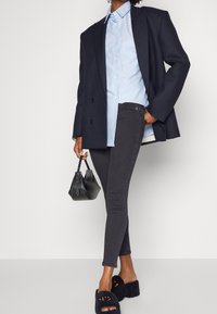 Jeans negros de corte ajustado, combinados con una camisa azul claro y un blazer negro estructurado. Completan el conjunto unas sandalias negras de plataforma esponjosas y un pequeño bolso negro.