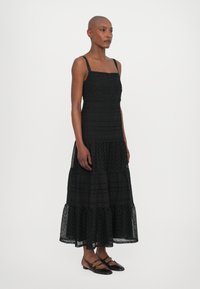 Rochie neagră cu volane, având un corset ajustat, bretele subțiri și modele decorative din dantelă. Asortată cu pantofi negri fără toc.