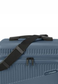 Valigia da viaggio rigida in materiale blu testurizzato, dotata di manico nero, tracolla regolabile e chiusura a doppia zip con logo.