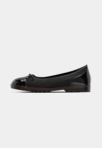 Black ballet flat shoe with patent leather cap toe, bow detail, and textured sole. Smooth upper material, low-profile design.