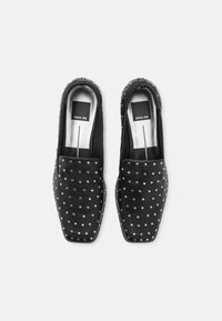 Black leather loafers featuring a square toe design, adorned with silver studs for texture and detail, with a smooth black interior.