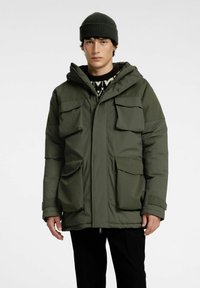 Olivgrön parkasjacka med huva, två stora bröstfickor och dubbla sidfickor. Tillverkad av ett slätt, hållbart tyg med en avslappnad passform.