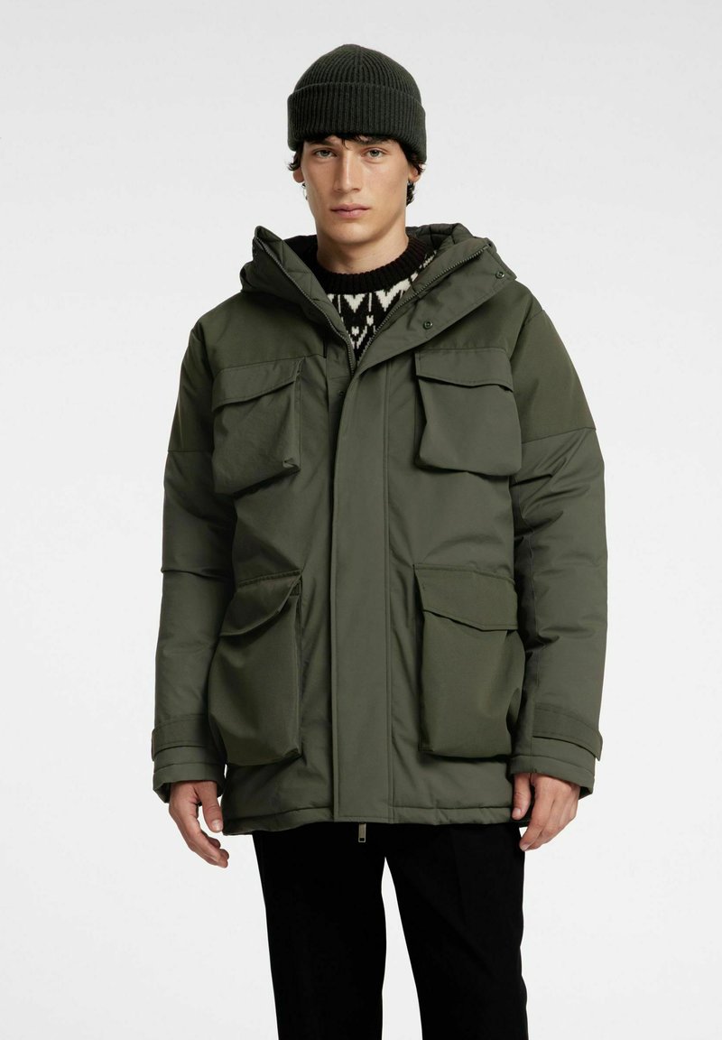 Olivgrön parkasjacka med huva, två stora bröstfickor och dubbla sidfickor. Tillverkad av ett slätt, hållbart tyg med en avslappnad passform.