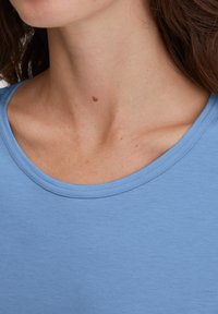 Lichtblauw T-shirt met een ronde hals, gemaakt van zachte stof. Heeft een gladde textuur en een relaxte pasvorm. Zichtbaar nekgedeelte.