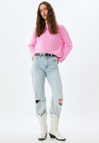 Rosa ribbad stickad tröja, ljusblå slitna jeans med trasiga knän, svart bälte med silverdetaljer och vita cowboyboots.