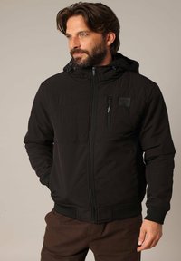 Zwarte hoodie jacket met een ritssluiting, gewatteerde textuur aan de voorkant, verstelbare capuchon en elastische manchetten. Bevat een borstzak.