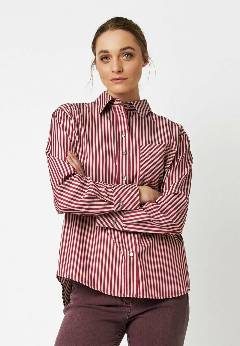 Red and white striped button-up shirt with a pointed collar and single chest pocket; tailored fit with long sleeves and slight high-low hem.