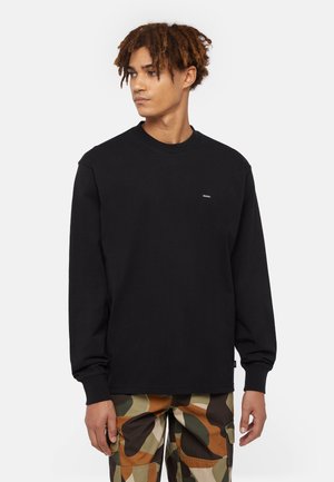 Sort langærmet t-shirt i blødt bomuld, med rund hals og et lille logo-patch på brystet, parret med camouflage cargo-bukser.
