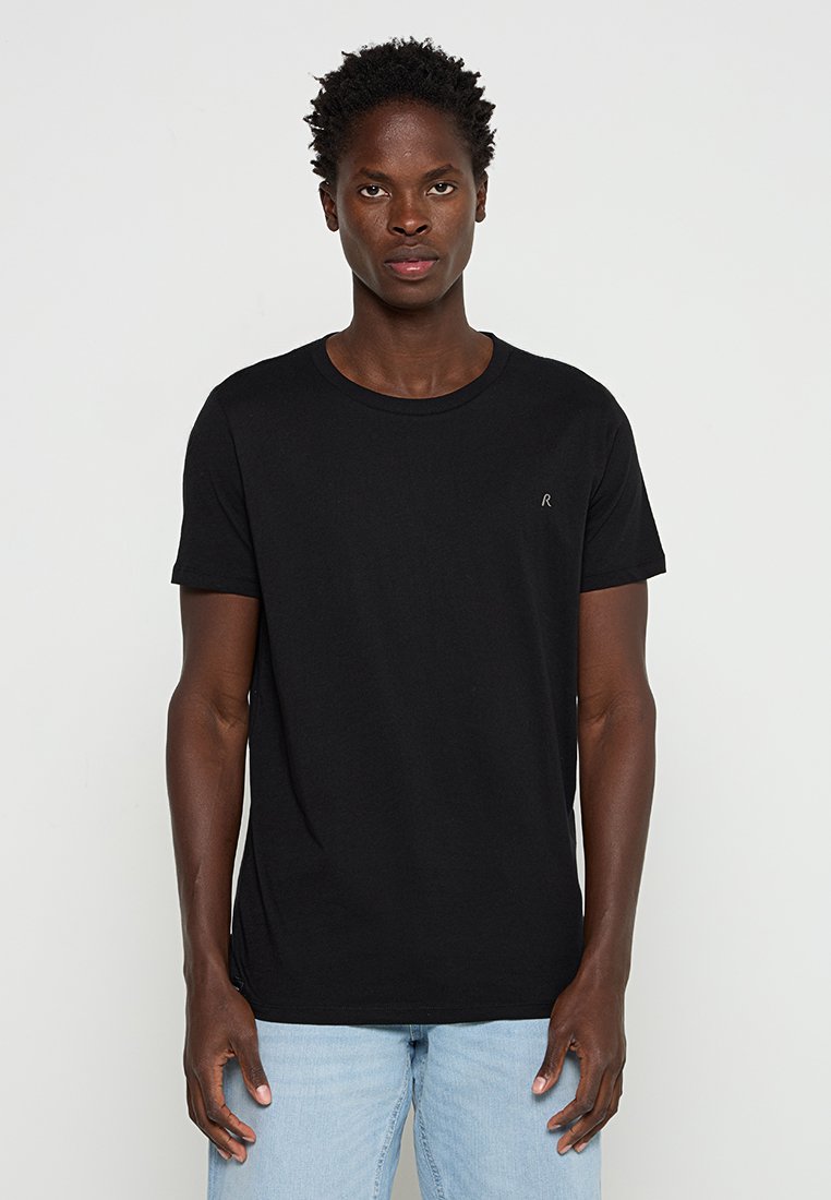 Czarny bawełniany t-shirt z okrągłym dekoltem, krótkimi rękawami i małym logo na lewej piersi. Połączony z jasnoniebieskimi dżinsami.