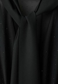 Czarna bluzka z szyfonu z wiązaniem przy szyi, teksturowaną tkaniną i rozrzuconymi srebrnymi kropkami jako akcentem. Miękko układająca się, lekka w wyglądzie.