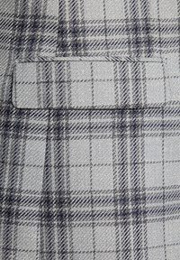 Szara tkanina w kratę o fakturowanym splocie, z ciemnonawowym i jasnoszarym wzorem. Zawiera małą kieszonkę na powierzchni.