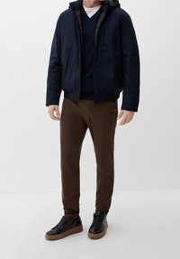 Marineblå pufferjakke med en brun foring, lynlås-lommer, parret med en mørk trøje og brune slim-fit bukser. Sorte sneakers med en tan sål.