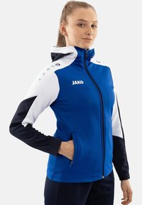 Giacca sportiva blu con accenti bianchi e neri, chiusura con zip e cappuccio. Presenta il logo "JAKO" e tasche laterali. Tessuto liscio e elasticizzato.