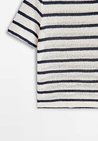 Sweter na drutach w kremowym kolorze z granatowymi poziomymi paskami. Posiada krótkie rękawy i luźny krój. Tkanina jest teksturowana i oddychająca.