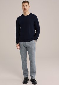 Jūrų laivyno megztinis, pilki raštuoti kelnių ir juodos loafer stiliaus bateliai. Paprastos apvalios kaklo dizainas ir riboti rankogaliai. Lygi audinio tekstūra.