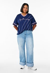 Navy short-sleeve t-shirt with a V-neck, featuring white and red stripes, and the text "togetherness" in a cursive font. Paired with light blue wide-leg jeans.