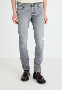 Jean gris à coupe slim, doté de cinq poches, léger d�élavage et détails de couture. Associés à des mocassins bordeaux foncé.