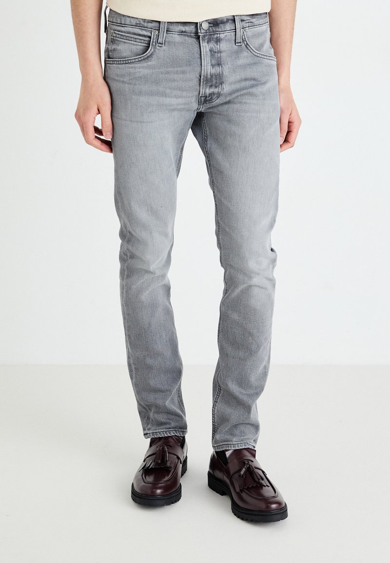 Jean gris à coupe slim, doté de cinq poches, léger délavage et détails de couture. Associés à des mocassins bordeaux foncé.
