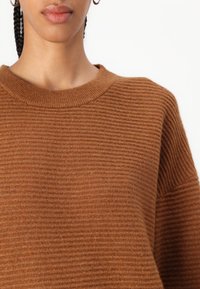Brown ribbed knit sweater with a round neckline, soft texture, and relaxed fit, featuring distinct horizontal lines and loose sleeves.