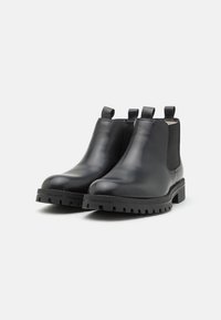 Bottines Chelsea en cuir noir avec panneaux latéraux en élastique, bout rond, semelles en caoutchouc plates et languettes pour un enfilage facile.
