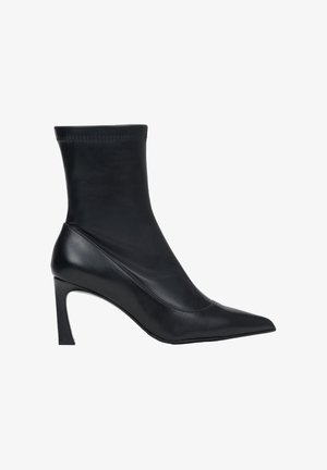 Zwarte enkelhoge hakken van glad leer. Ze hebben een aangesloten bovenwerk en een spits toelopende neus. De hak is slank en ongeveer 10 cm hoog.