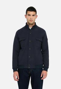 Marineblaue Jacke aus glattem Stoff, mit Stehkragen, frontaler Knopfleiste und zwei Brusttaschen mit Klappen.