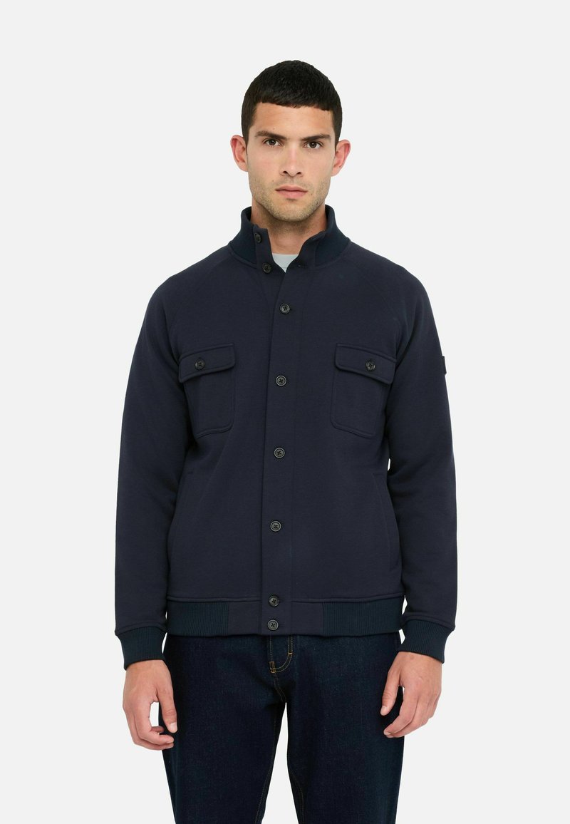Marineblaue Jacke aus glattem Stoff, mit Stehkragen, frontaler Knopfleiste und zwei Brusttaschen mit Klappen.