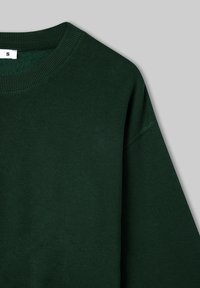 Zielona bluza z okrągłym dekoltem, długimi rękawami i miękką fakturą. Etykieta rozmiaru widoczna przy kołnierzu.