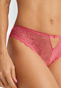 Κοντινό πλάνο ενός ατόμου που φοράει ροζ δαντελένιο εσώρουχο με κεντητά λουλουδάτα σχέδια και μικρή κορδέλα στη μπροστινή ζώνη μέσης.