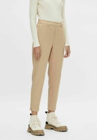 Beige kalhoty s vysokým pasem, bočními švy a slim fit, spárované s krémovými kotníkovými botami se šněrováním a silnými podrážkami.