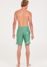 Groene zwemshorts van lichtgewicht stof, met een wit streep patroon en een achterzak met de tekst "PRO TEST".