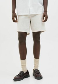 Pantalones cortos de lino color beige claro, con un corte relajado. Llevados con calcetines crema y zapatos marrón oscuro con un frente decorativo.