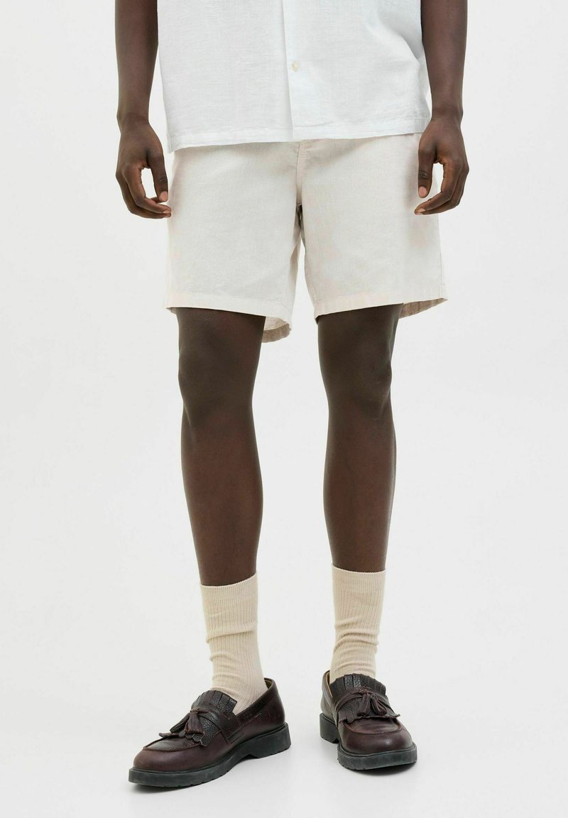 Pantalones cortos de lino color beige claro, con un corte relajado. Llevados con calcetines crema y zapatos marrón oscuro con un frente decorativo.