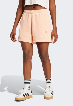 Pantaloni sportivi pesca con vita elastica e tasche laterali, abbinati a calze a righe bianche e nere e a scarpe Adidas.