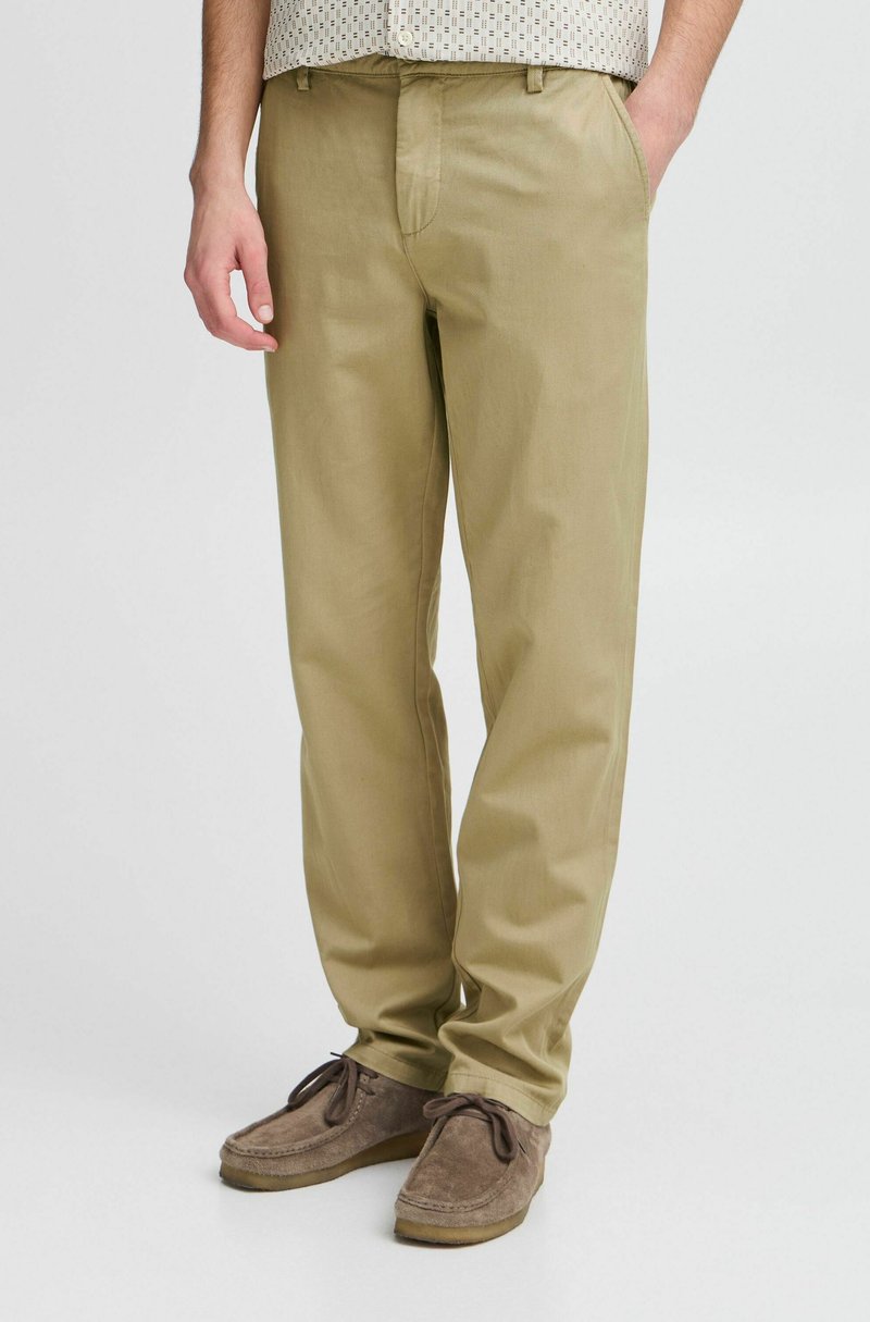 Beige Baumwollhosen mit geradem Schnitt, flachem Frontbereich, schrägen Taschen und lässigem Fit, kombiniert mit braunen Wildlederschuhen.