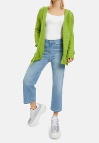 Cardigan verde lavorato a maglia, canotta bianca, jeans cropped azzurri chiari e sneakers iridescenti. Tessuto lavorato a maglia e vestibilità comoda.