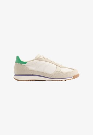 Beżowe sneakersy z gładką cholewką i zamszowymi akcentami, z zielonym zakładką na pięcie, fioletową podeszwą środkową i teksturowaną gumową podeszwą.
